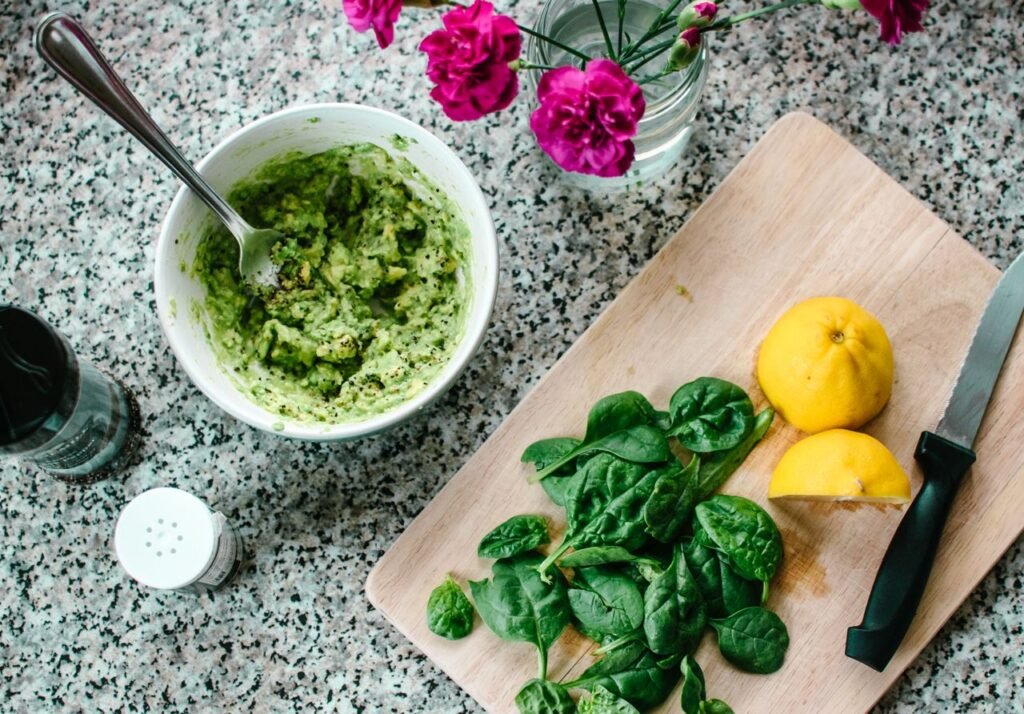 A vibrant kitchen scene with fresh guacamole, spinach, and lemons on a cutting board for healthy meal prep.