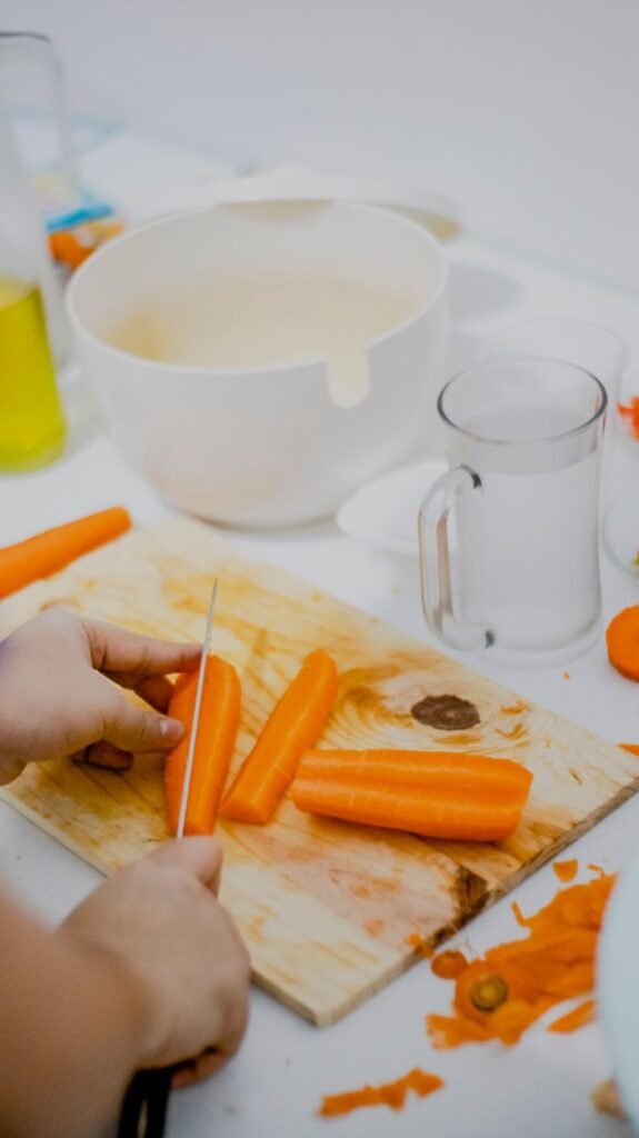 Close-up of hands slicing vibrant orange carrots on a wooden cutting board in a kitchen setting.