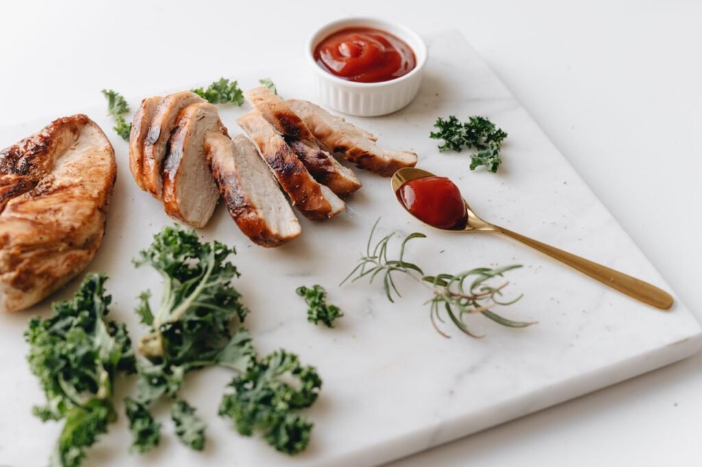 Sliced grilled chicken with greens and ketchup on a marble board, perfect for a healthy meal.
